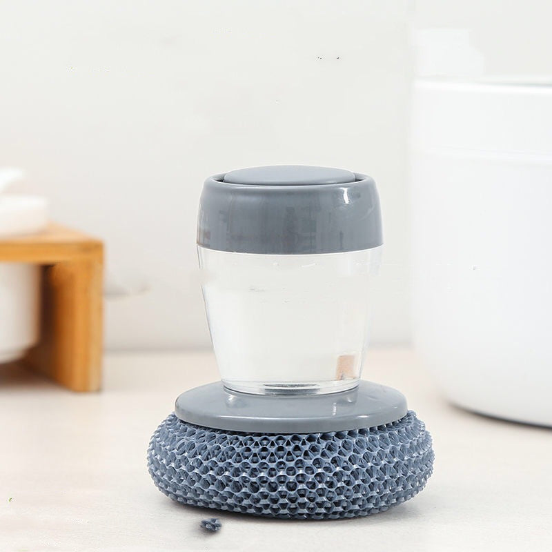 Gray soap dispenser brush with textured scrubber on a light kitchen countertop