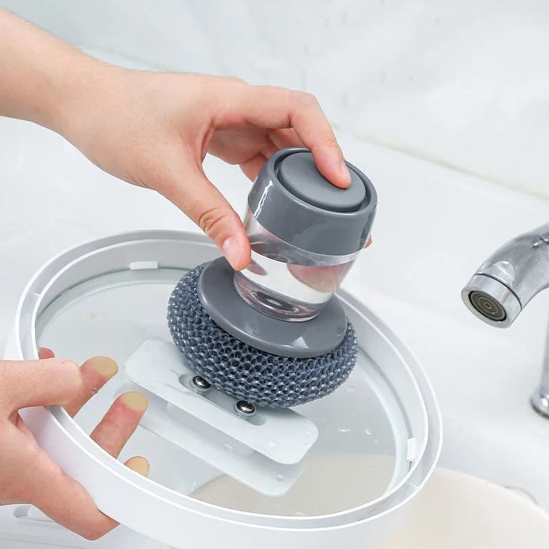 Hand using a soap dispensing sponge brush to clean a glass pot lid at a sink