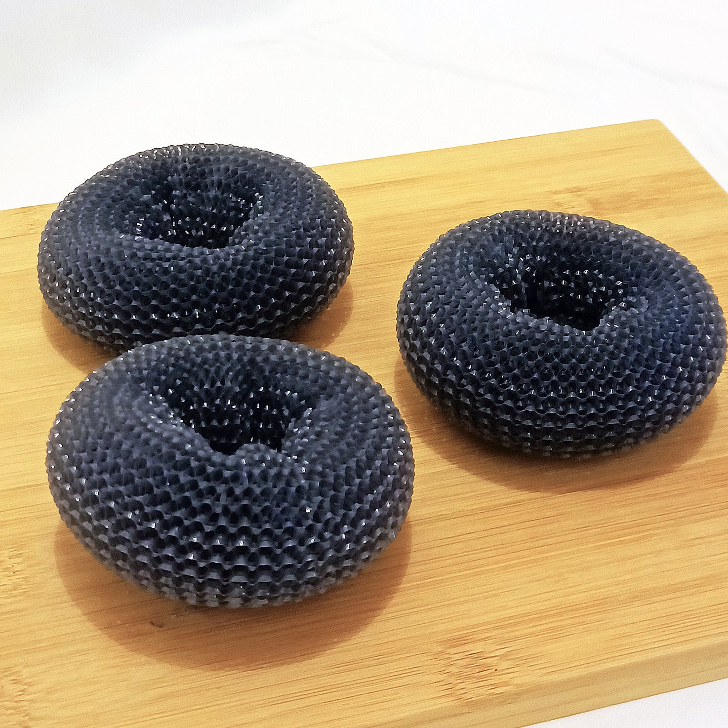 Three black mesh kitchen scrubbers on a wooden board
